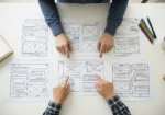 Team reviewing website wireframe sketches on a desk, representing how sitemaps and wireframes reduce redesign risk, scope creep, and planning gaps.