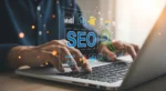 Hands using a laptop with SEO dashboard graphics, representing canonicalization, redirects, broken links, and technical SEO fixes that protect site health.