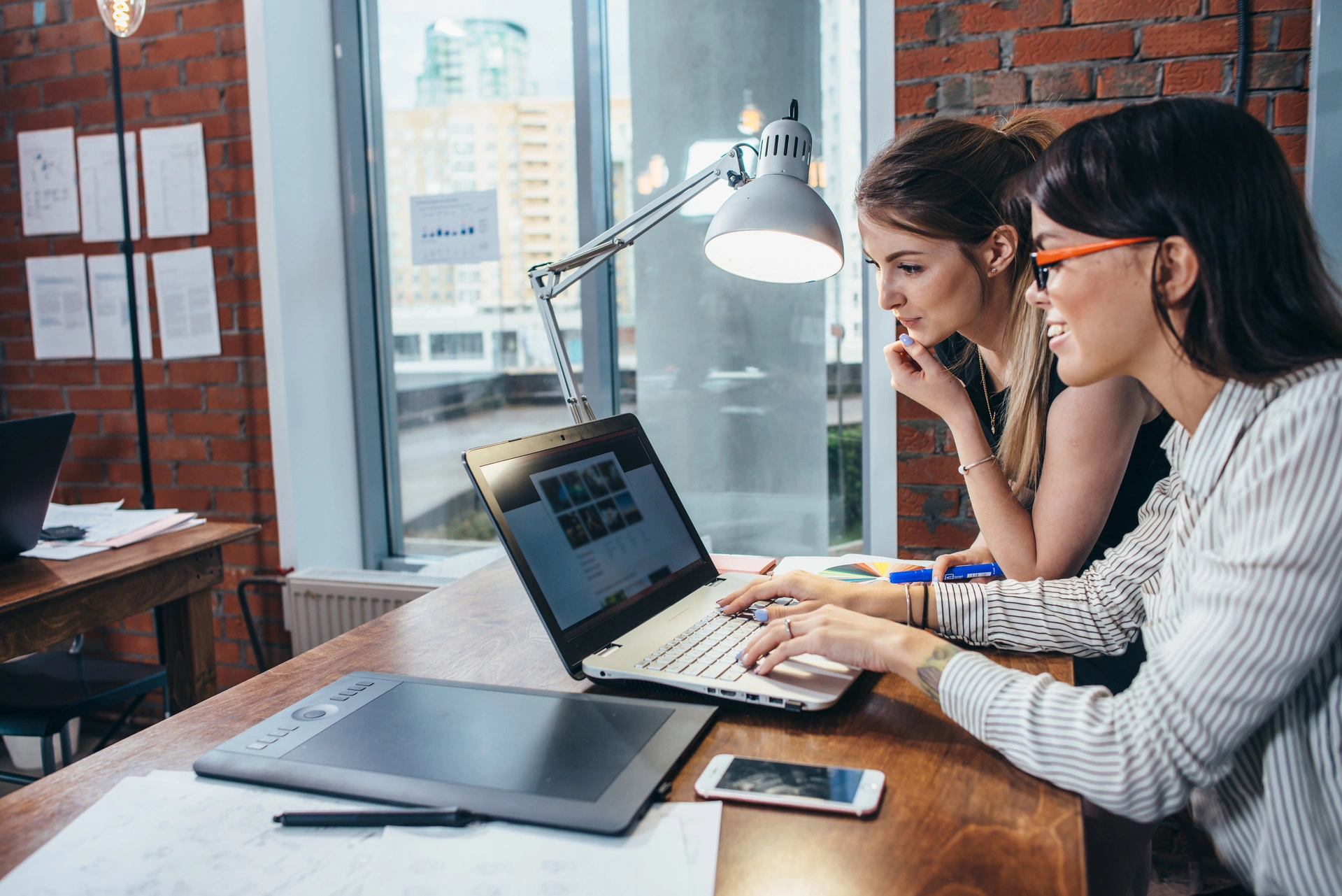 Two designers reviewing a website layout on a laptop while discussing user experience and site structure in a creative office