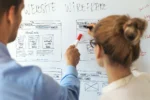 UX designers creating website wireframes on a whiteboard while planning layout, navigation, and user interface structure