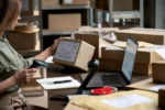 Ecommerce seller scanning a package beside a laptop and shipping boxes