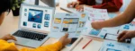 Design team reviewing website interface layouts and wireframes while planning digital product design on laptop and printed mockups